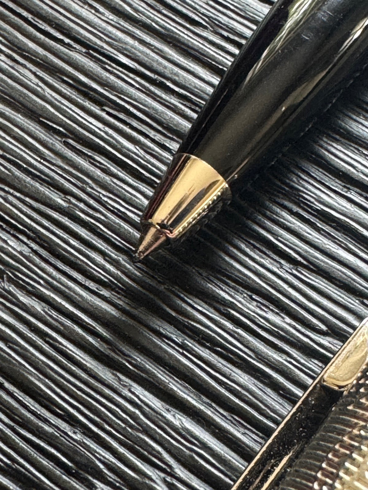 Detailed view of pen tip and grip section, showing gold-colored band and black cone-shaped ballpoint nib
