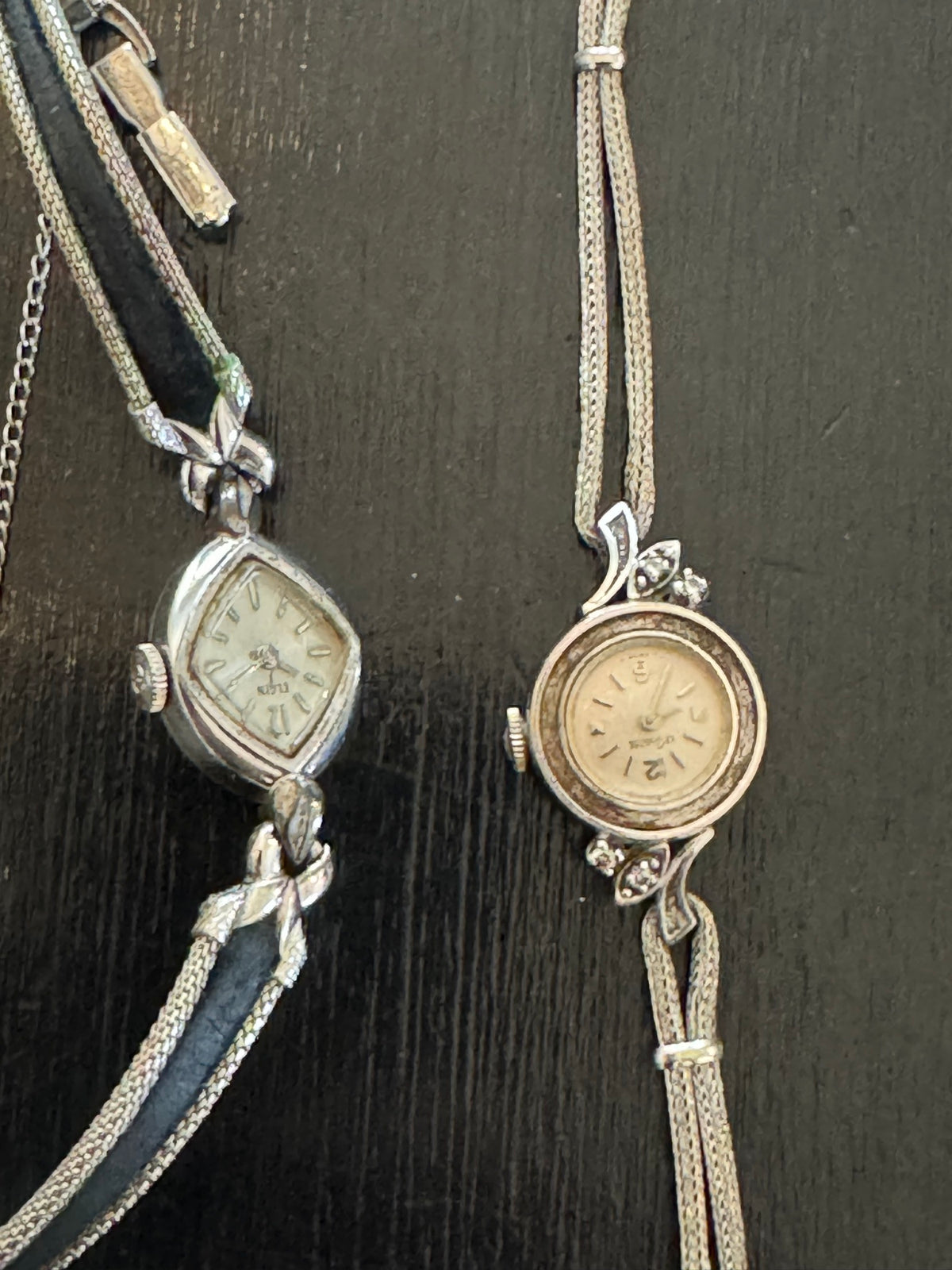 Two vintage silver-toned ladies' cocktail watches on fabric straps displayed against dark wooden background