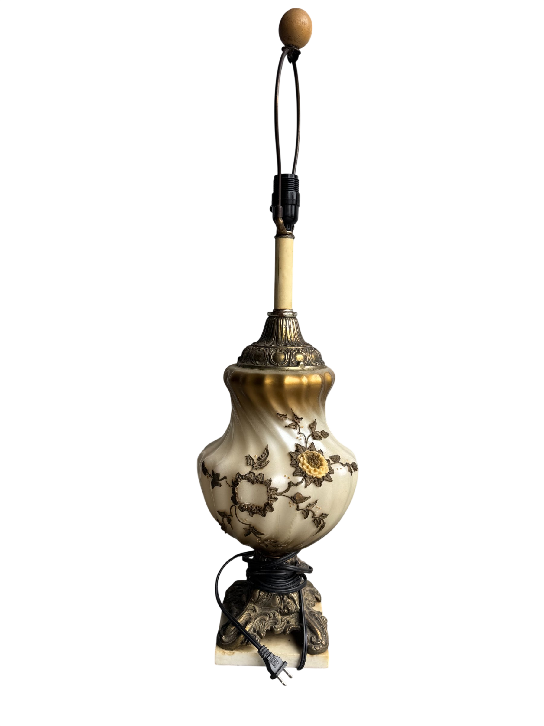 Full view of vintage gilt porcelain table lamp with cream bulbous body, floral relief design, ornate brass fittings, wooden finial, and black cord
