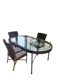 Oval glass-top dining table with dark metal frame and five woven resin wicker armchairs in sunlit screened porch