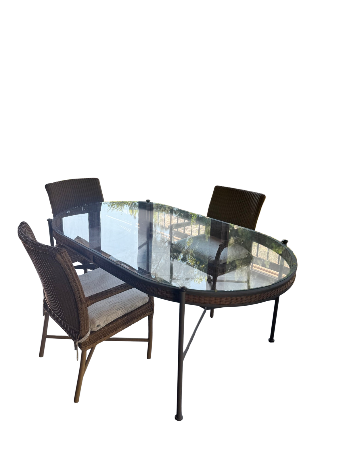 Oval glass-top dining table with dark metal frame and five woven resin wicker armchairs in sunlit screened porch