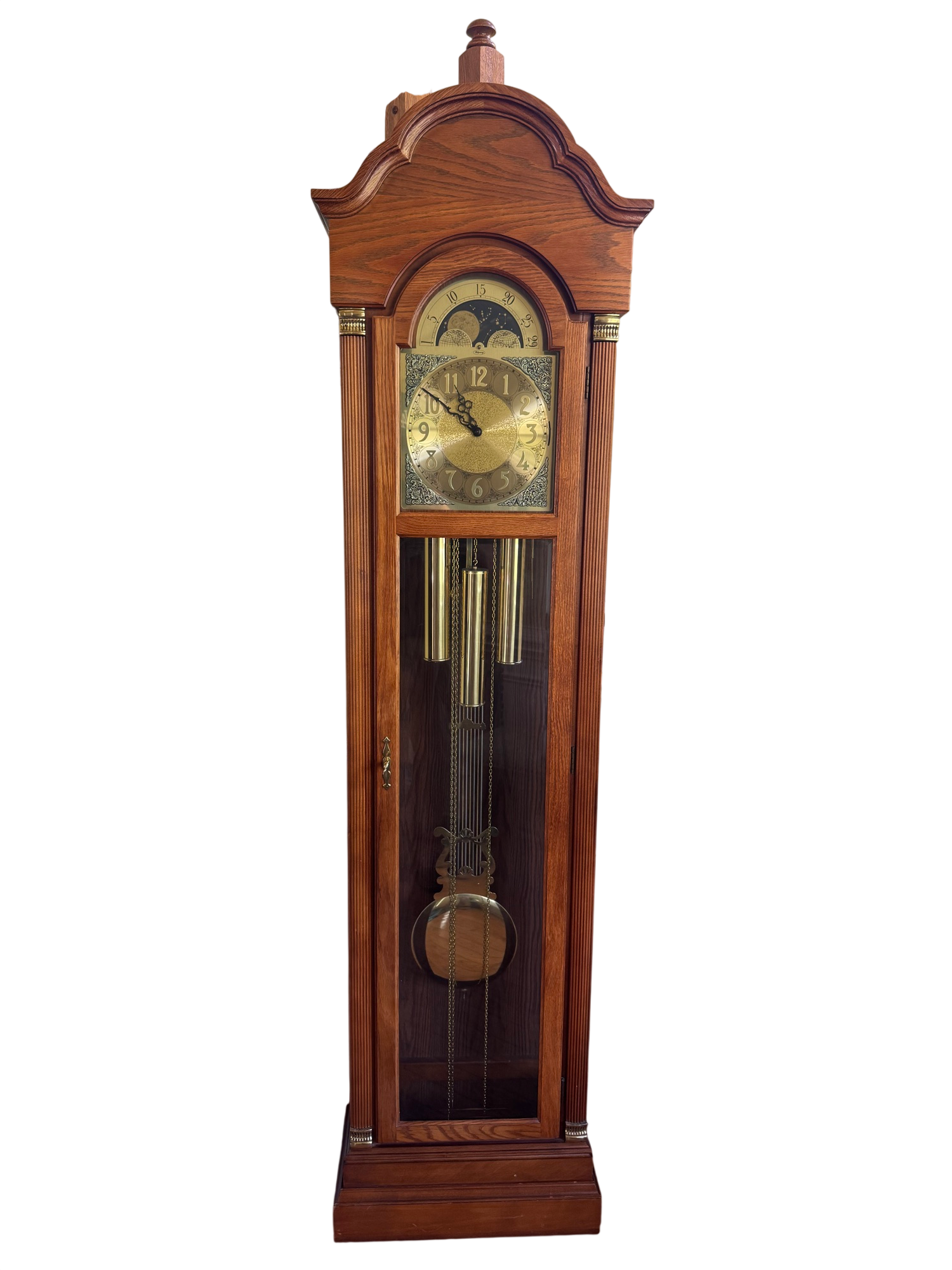 Full front view of oak case grandfather clock with arched pediment top, brass moon phase dial, and visible pendulum through glass door