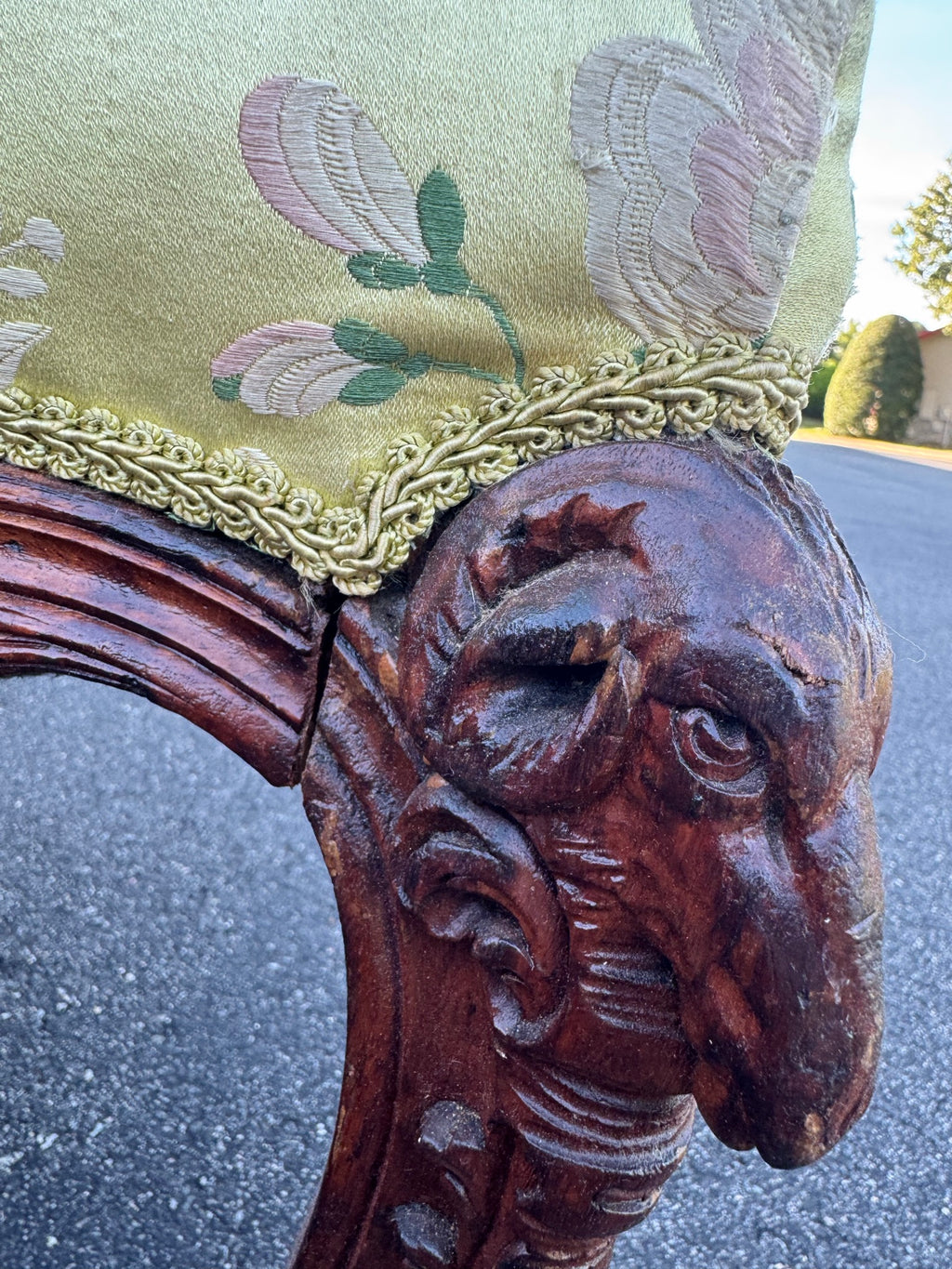 Carved ram's head at the knee of the chair's cabriole leg, the horn coiled around the ear and the muzzle carved in the round