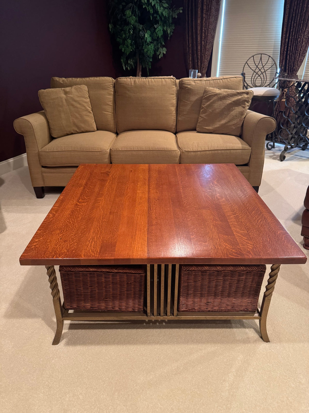 Quartersawn oak coffee table with wicker storage baskets, viewed from front, tan sofa and burgundy walls in background