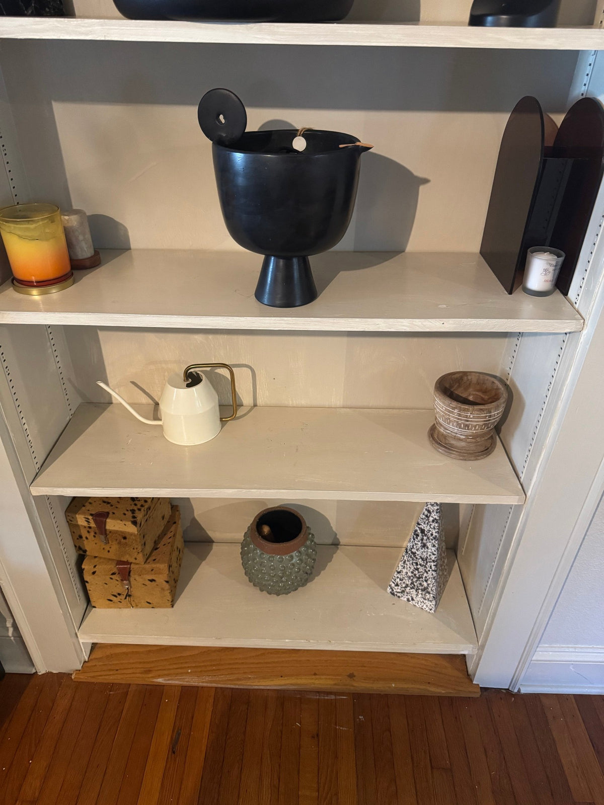 Footed black vessel, watering can and boxes on the lower shelves