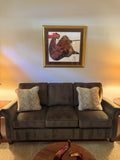 Olive brown microfiber three-seat sofa with two patterned throw pillows beneath framed artwork