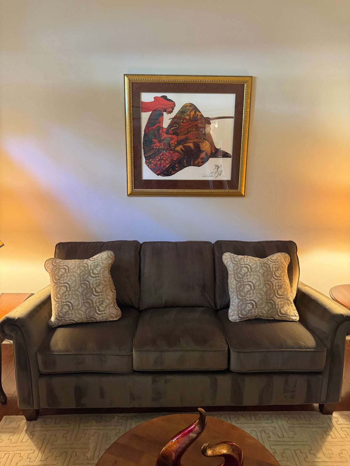 Olive brown microfiber three-seat sofa with two patterned throw pillows beneath framed artwork