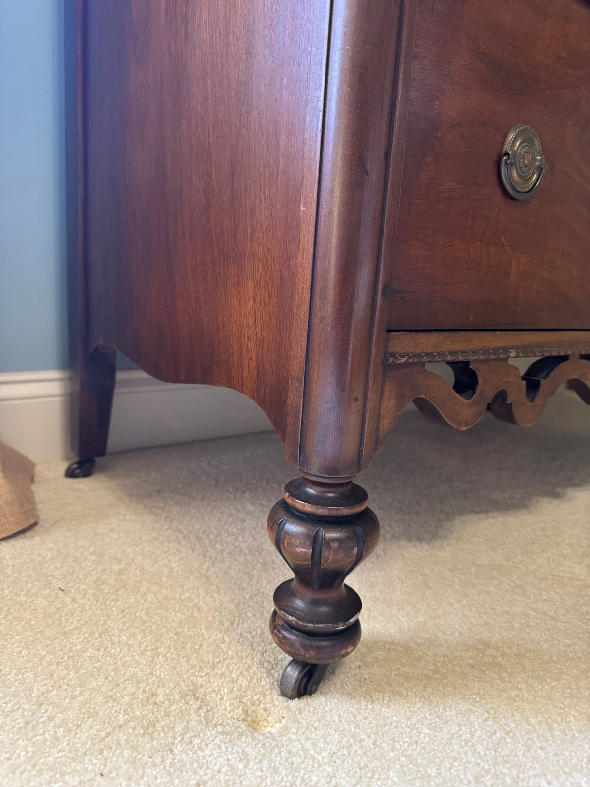 Close-up of turned wooden leg with caster wheel and decorative carved apron detail below