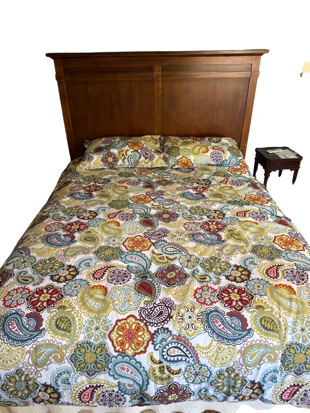 Queen bed with cherry finish panelled headboard, stepped crown molding, colorful paisley patterned bedding and pillows, sage green walls