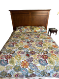 Queen bed with cherry finish panelled headboard, stepped crown molding, colorful paisley patterned bedding and pillows, sage green walls