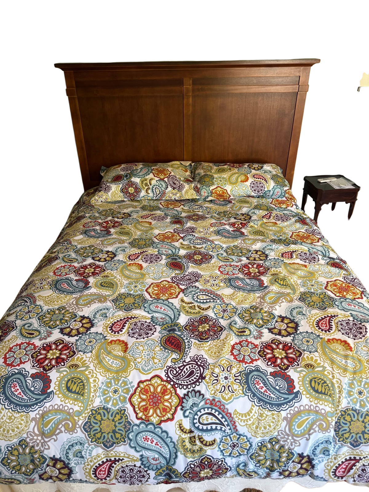 Queen bed with cherry finish panelled headboard, stepped crown molding, colorful paisley patterned bedding and pillows, sage green walls