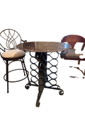 Round marble-top pub table with ornate scrolled iron pedestal base, viewed from above with two matching stools