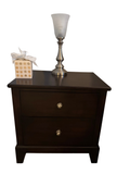 Espresso finish wood nightstand with two drawers and round brushed nickel knobs, shown with a lamp and tissue box on top