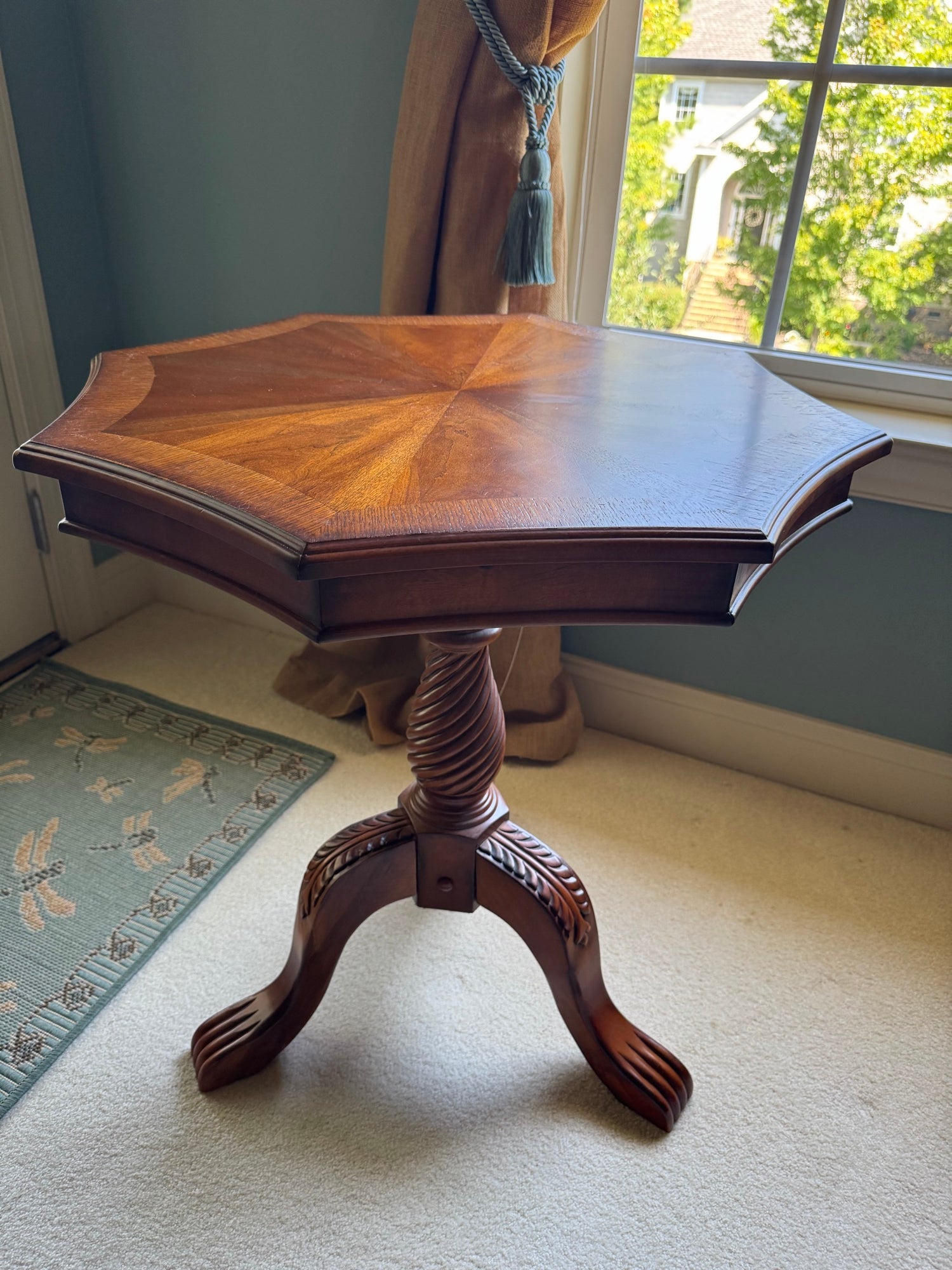 Octagonal wooden pedestal table with sunburst veneer top, carved tripod base with claw feet, viewed from above at angle