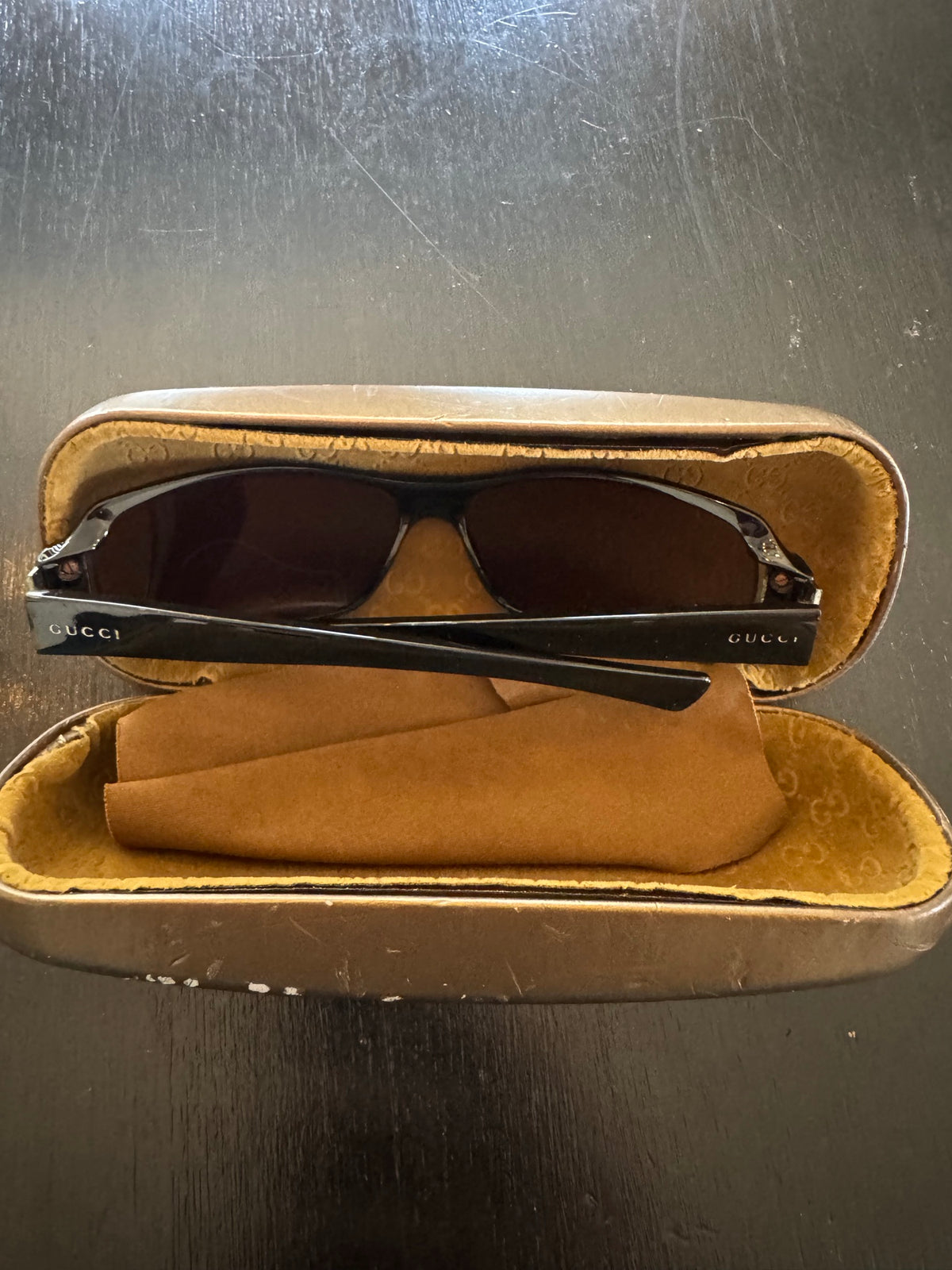 Gucci sunglasses with black frames and dark lenses in open tan velvet-lined case, showing interior view