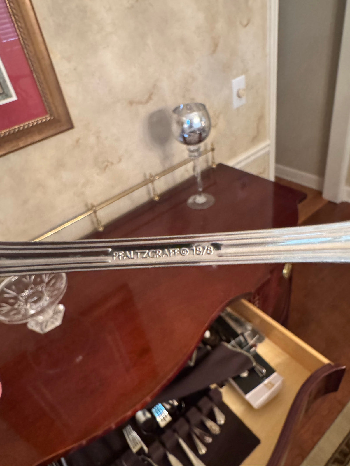 Fork handle marked Pfaltzgraff 18/8 next to a stemmed glass on a wood cabinet