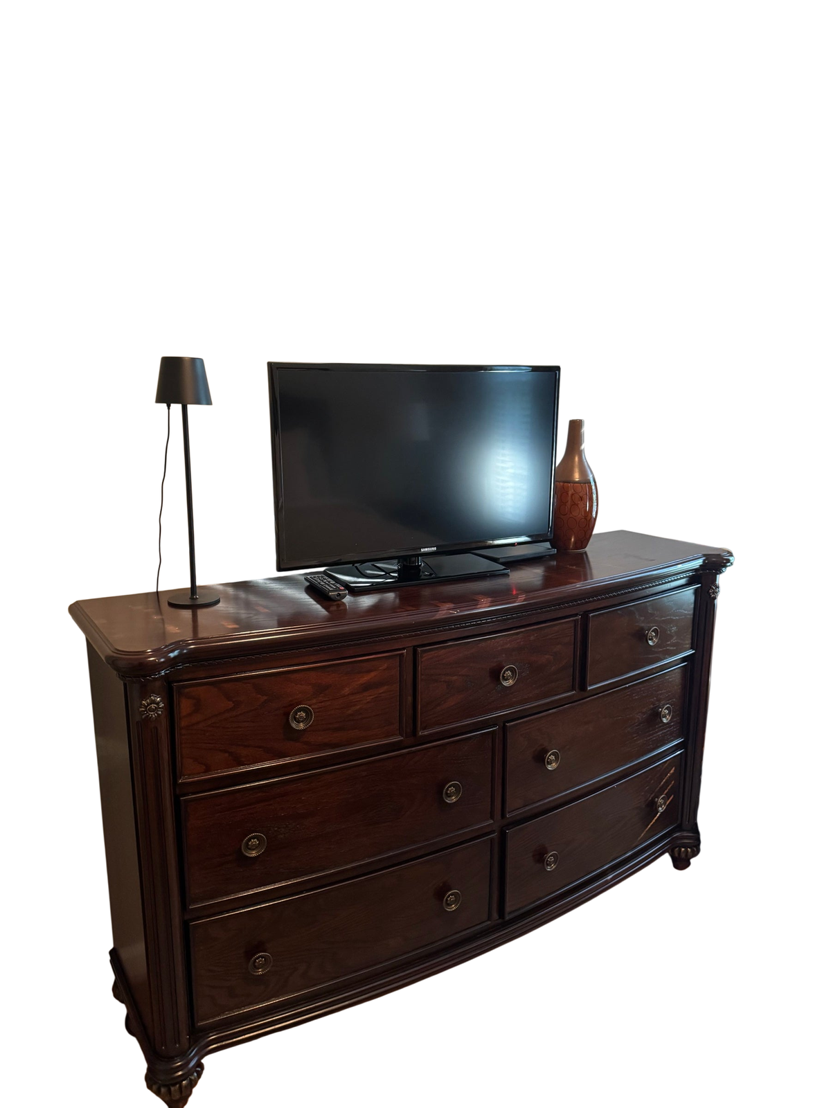 Dark cherry Havertys 7-drawer bowfront dresser with a Samsung TV, lamp, and vase on top, positioned against a wall beneath abstract art
