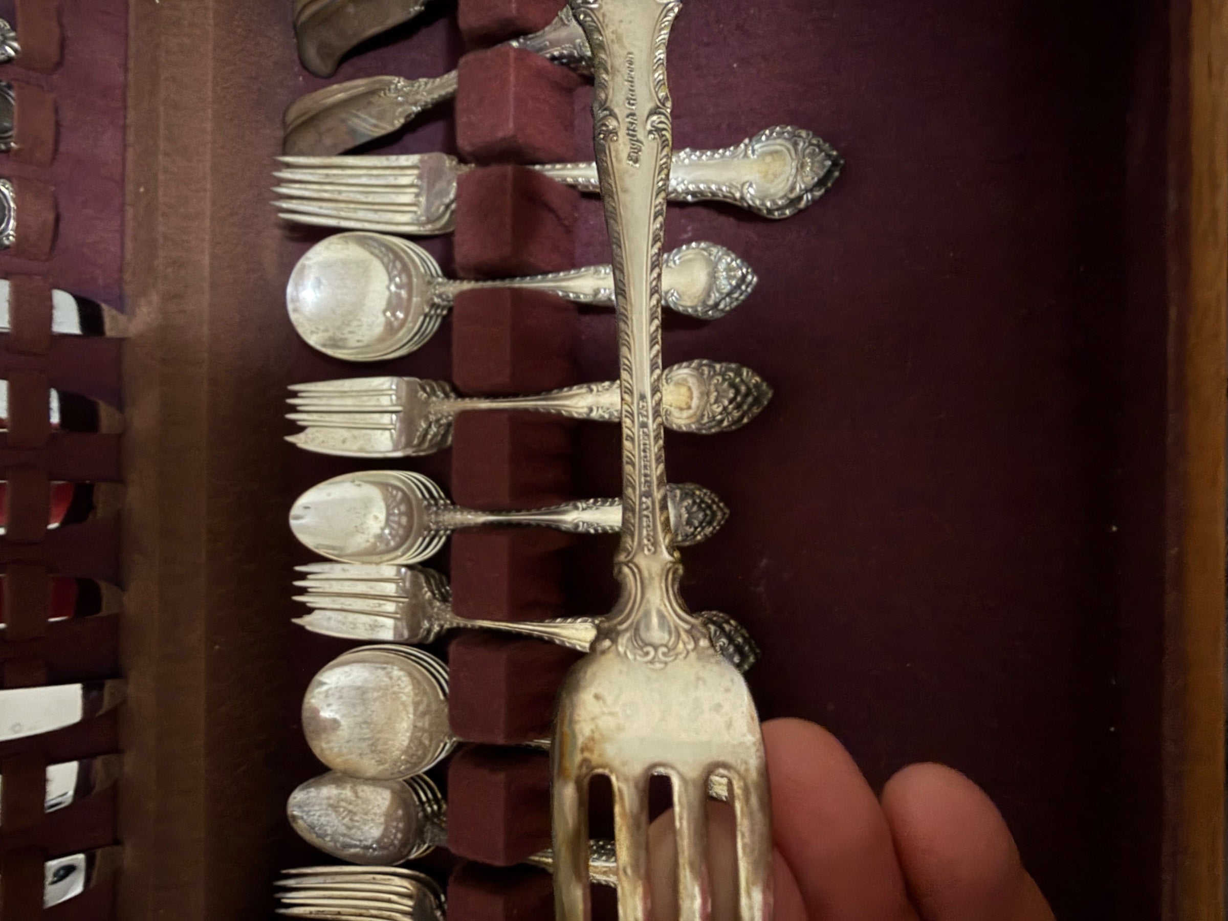 Flatware pieces arranged in chest showing alternating forks and spoons with ornate handles and polished silver bowls