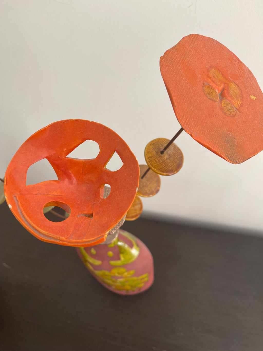 Detail of orange and red perforated metal flower forms with brown wood disc spacers on metal stems, artist signature visible at base
