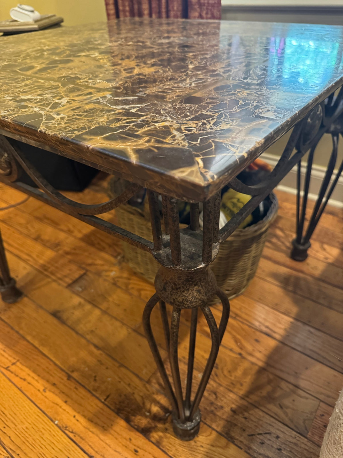 Angled view of table edge displaying marble top thickness, brass banding, and decorative iron leg with scroll detailing