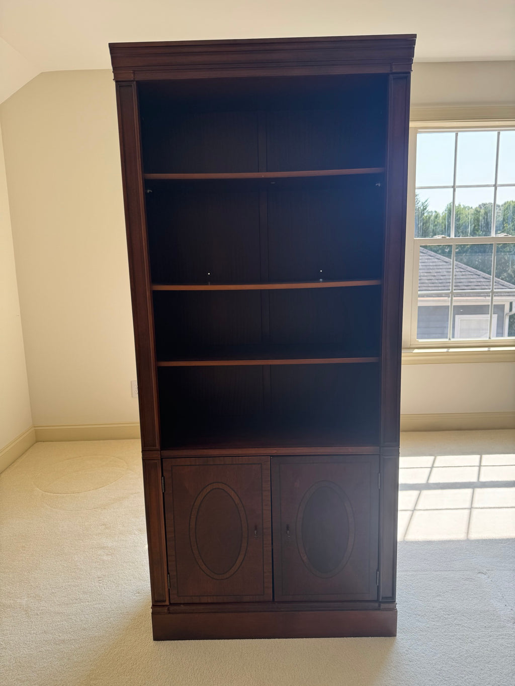 Tall mahogany bookcase with adjustable wood shelves in upper section and oval panel cabinet base, front view
