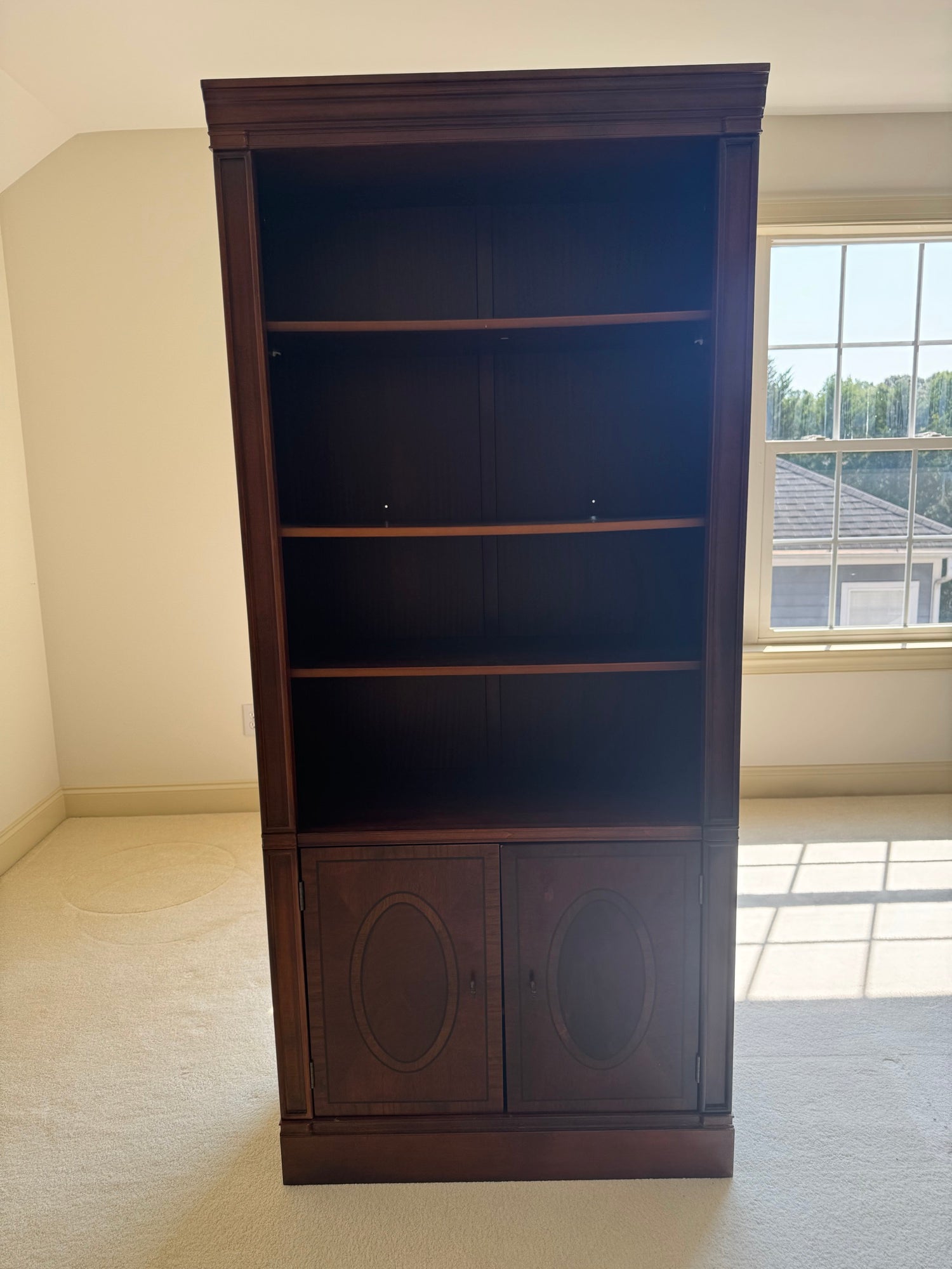 Tall mahogany bookcase with adjustable wood shelves in upper section and oval panel cabinet base, front view