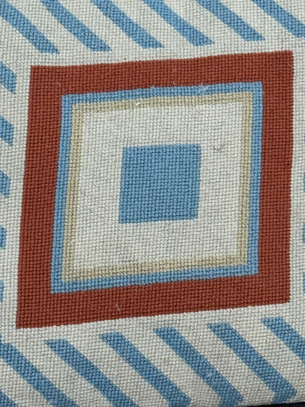 Close-up detail of needlepoint front showing concentric squares in rust, cream, light blue and darker blue with diagonal striped background pattern