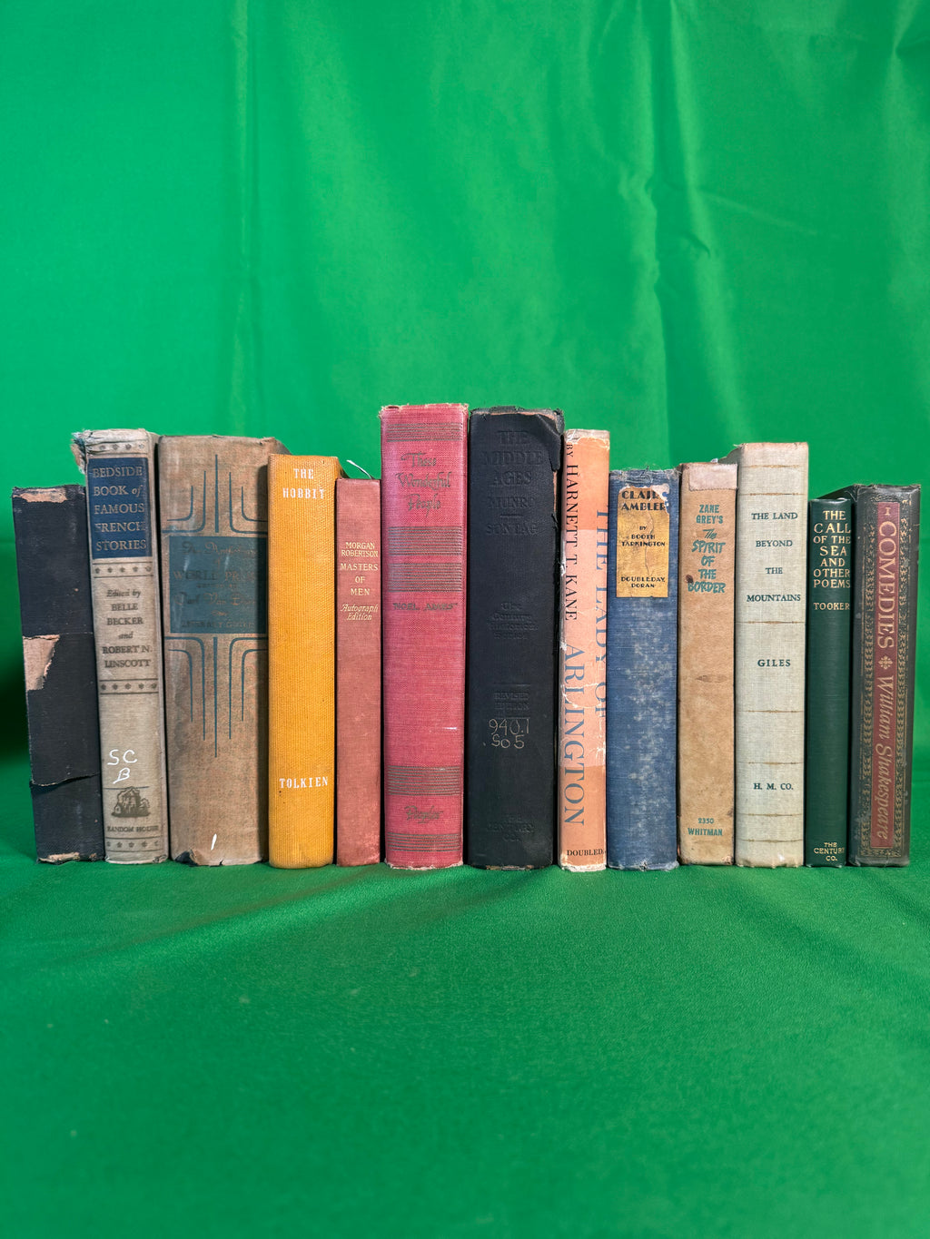 Vintage hardcovers stood spine-out on green cloth, including The Hobbit by J. R. R. Tolkien, Masters of Men from Morgan Robertson's Autograph Edition, and Zane Grey's The Spirit of the Border