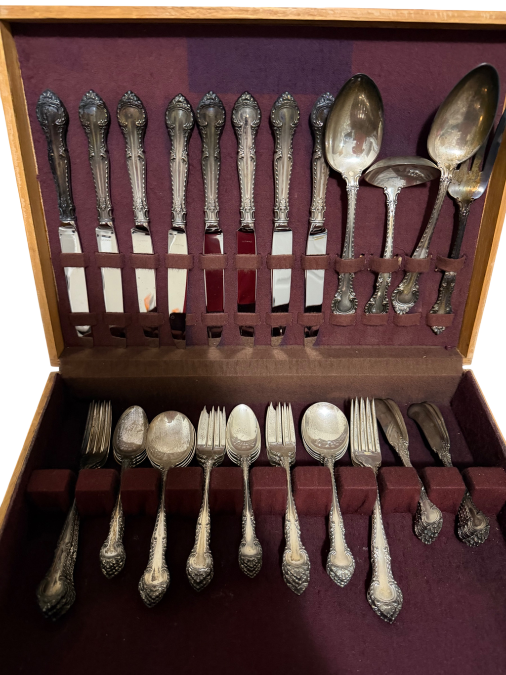Complete flatware set in wooden chest with purple velvet interior, displaying eight teaspoons, forks, spoons, and serving pieces with ornate handles