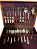 Complete flatware set in wooden chest with purple velvet interior, displaying eight teaspoons, forks, spoons, and serving pieces with ornate handles