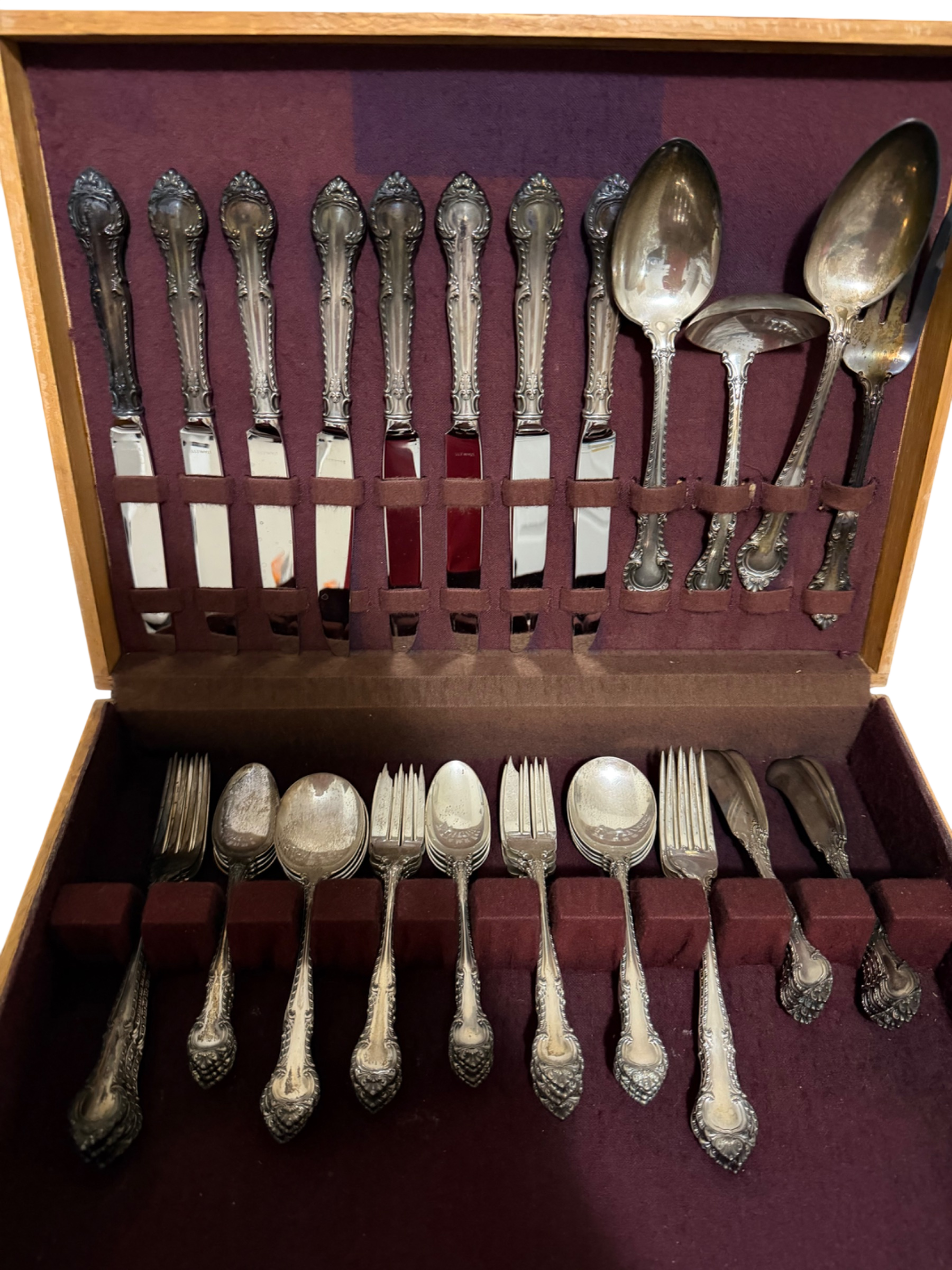 Complete flatware set in wooden chest with purple velvet interior, displaying eight teaspoons, forks, spoons, and serving pieces with ornate handles
