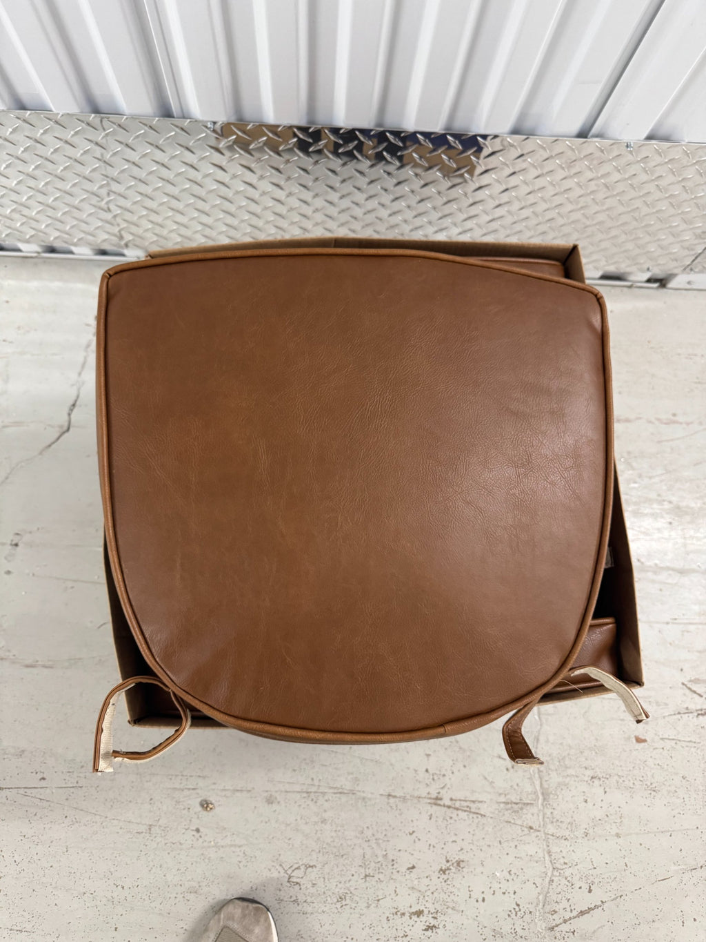 Brown vinyl chair seat cushion with rounded edges and tan fabric ties, viewed from front on concrete floor