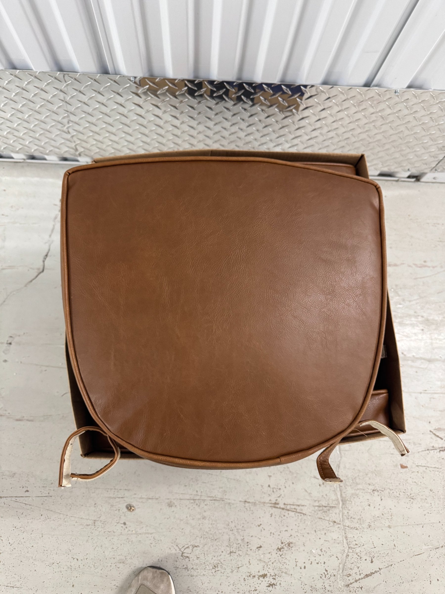 Brown vinyl chair seat cushion with rounded edges and tan fabric ties, viewed from front on concrete floor