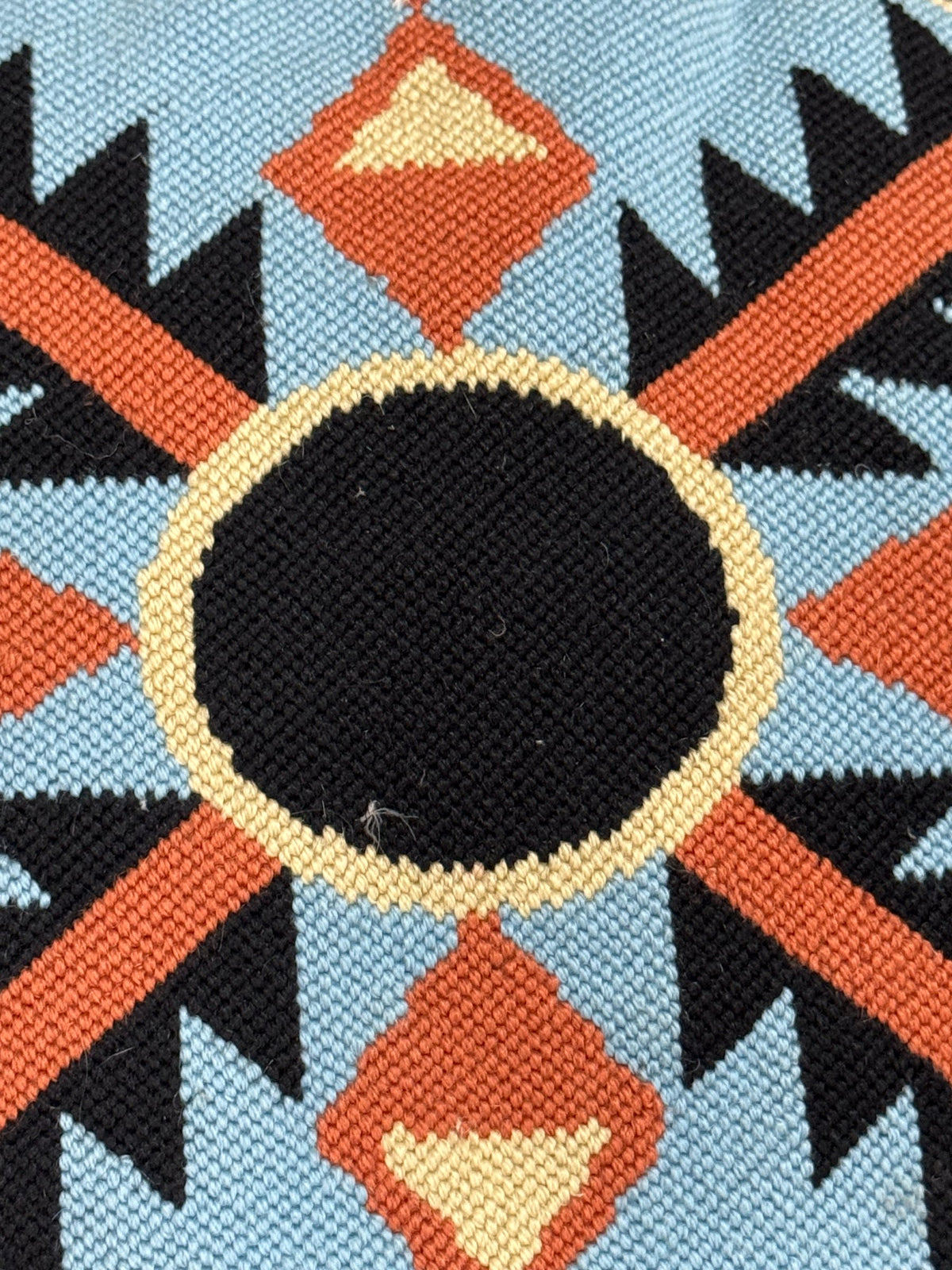 Close-up detail of needlepoint stitching showing cream-colored ring around central black circle with rust and black geometric pattern visible