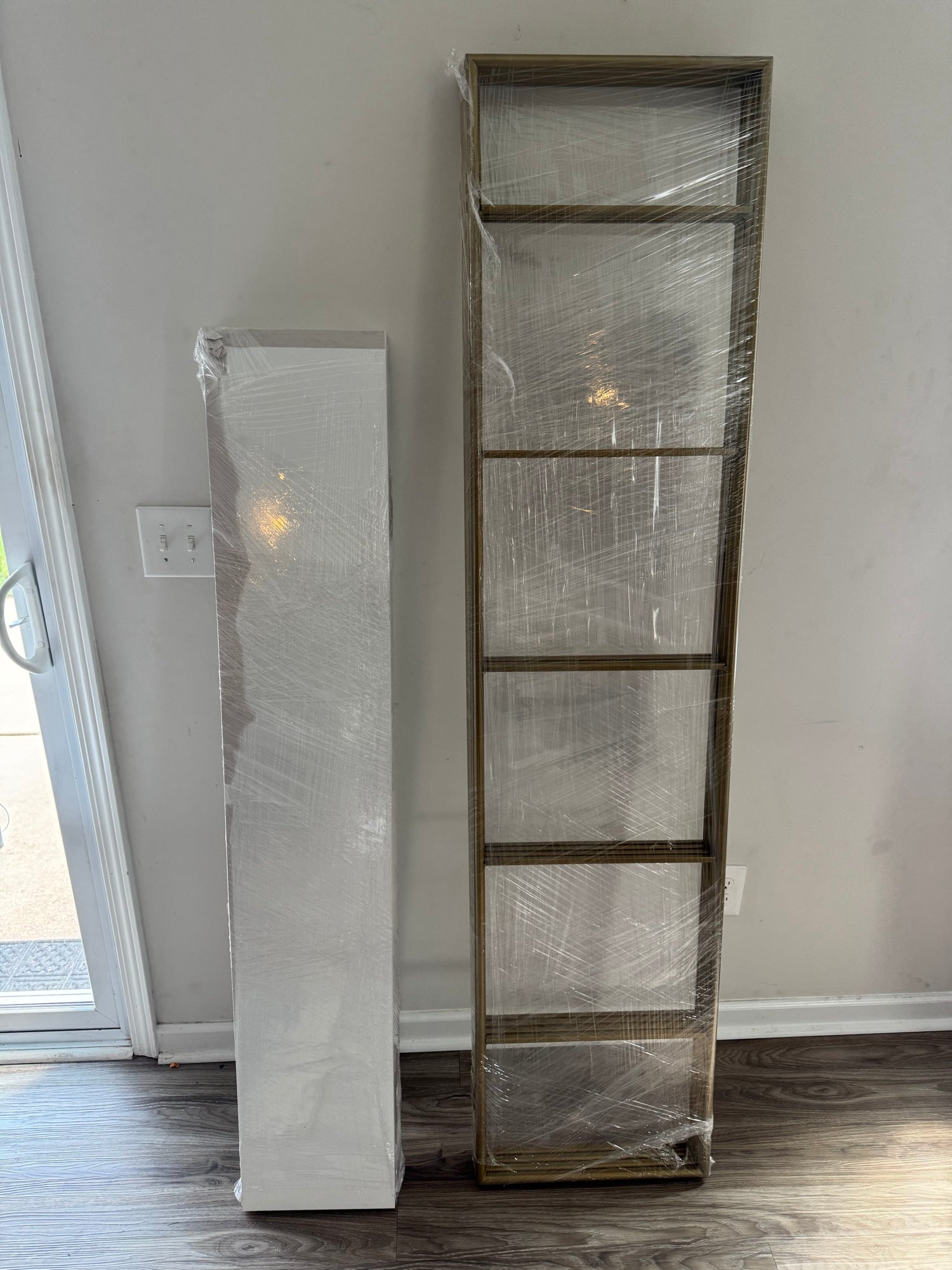 Tall narrow white wrapped bookcase and larger dark wood-framed shelving unit displayed side by side in room setting