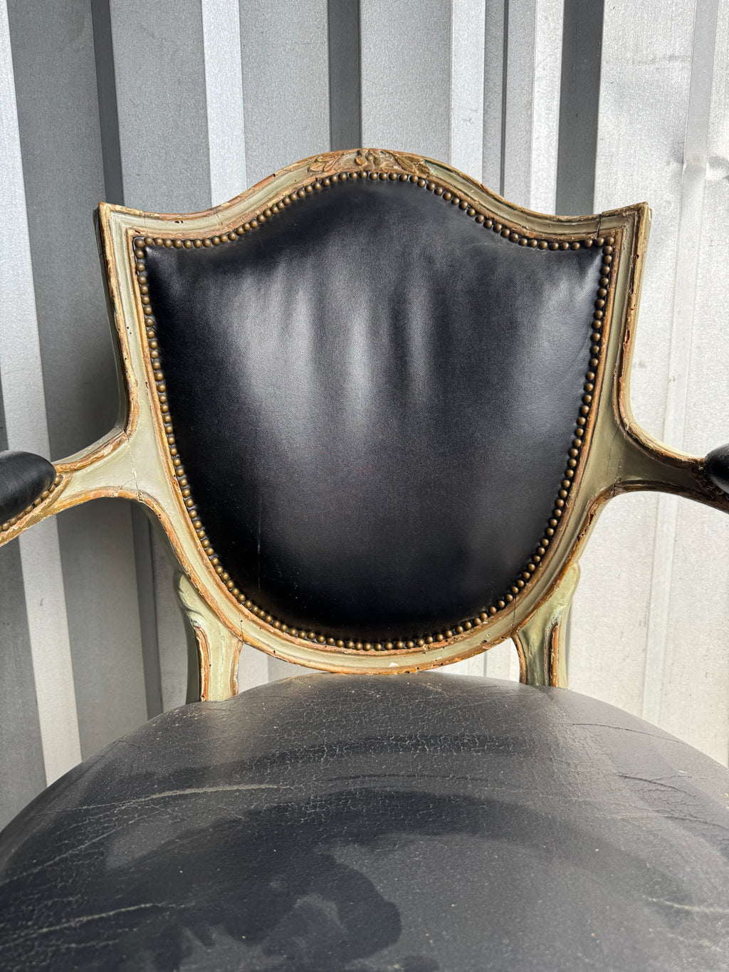 Close-up of chair backrest showing black leather upholstery with nailhead trim and curved painted wooden frame with gold accents