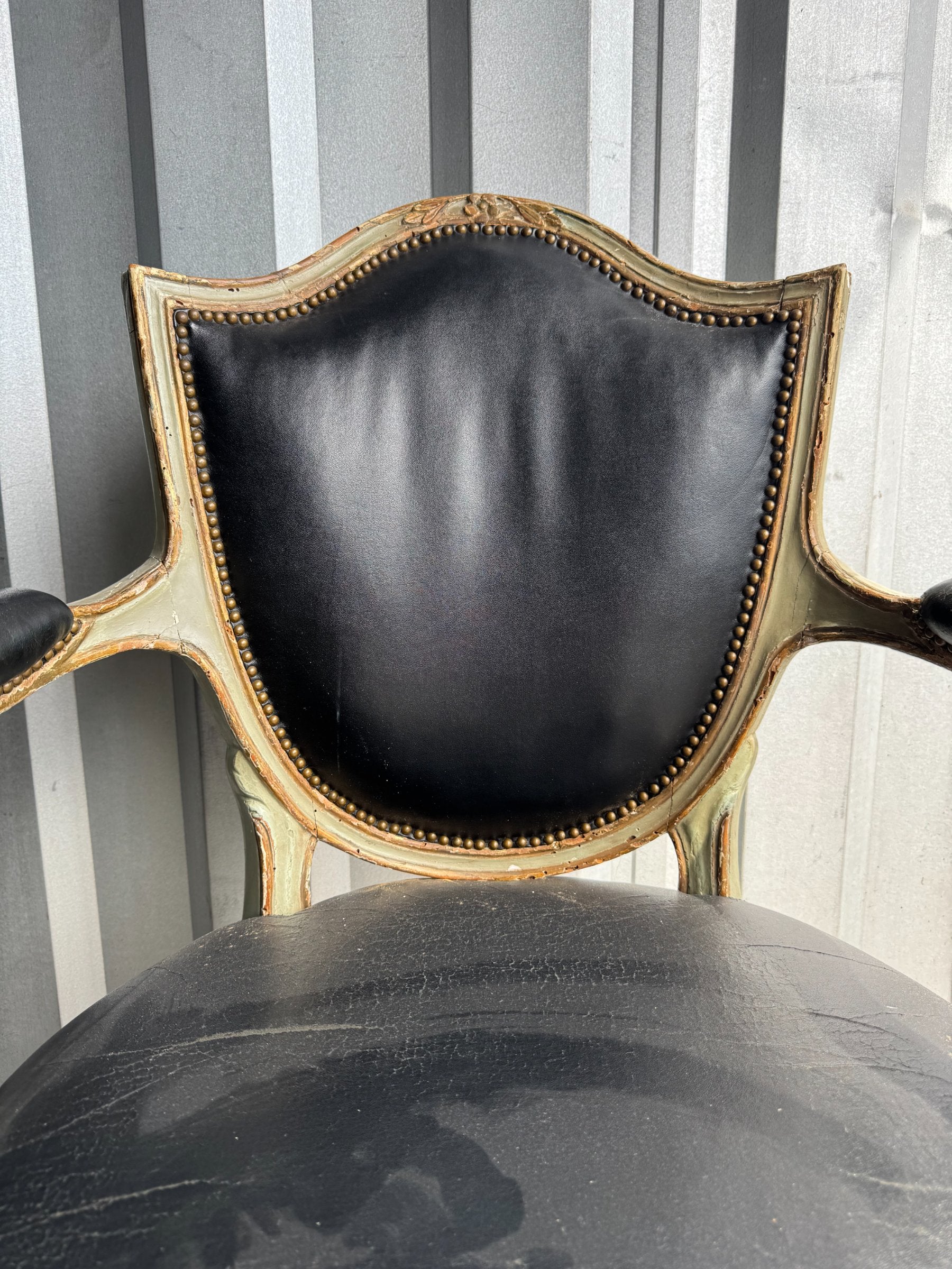 Close-up of chair backrest showing black leather upholstery with nailhead trim and curved painted wooden frame with gold accents