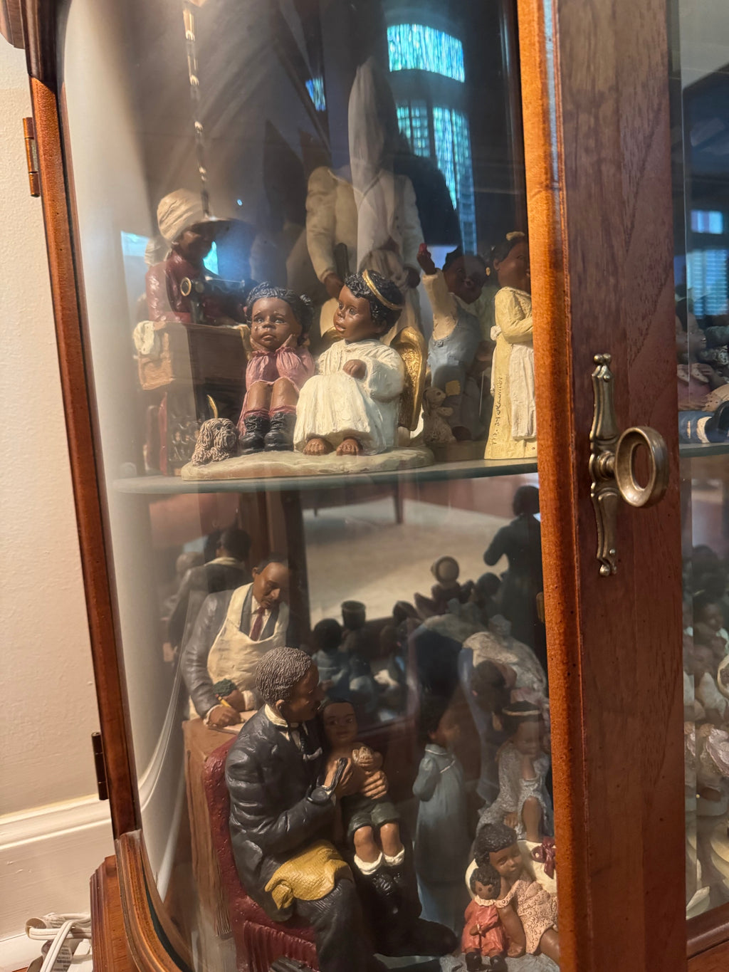 Curio cabinet shelves with All God's Children figurines including an angel, a girl at a sewing machine, and seated figures