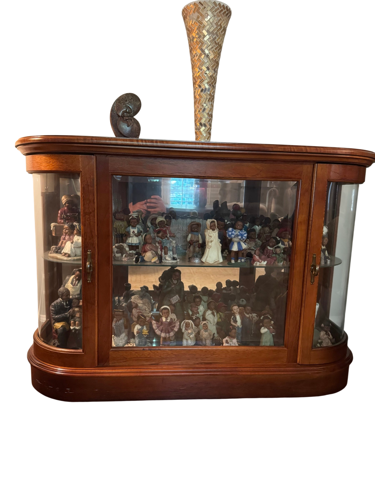 Cherry-finished bow-front curio cabinet with curved glass side panels, glass shelves, mirror backing, and brass door pulls, shown with a decorative vase and figurine on top.