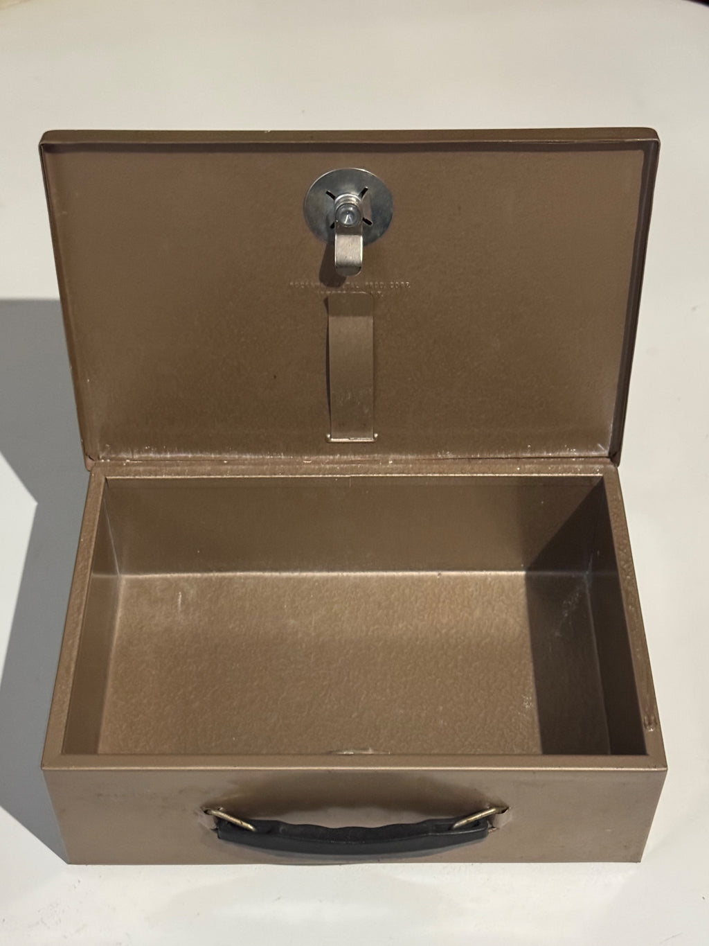 Open tan metal cash box interior showing empty compartment and chrome lock hardware from above