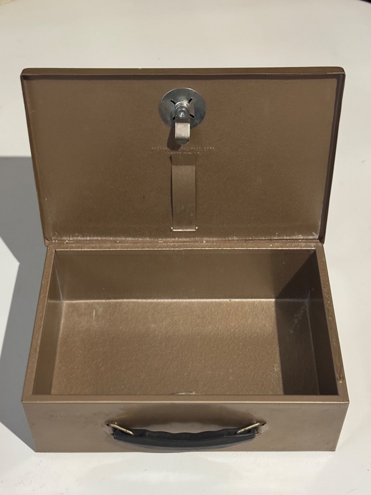 Open tan metal cash box interior showing empty compartment and chrome lock hardware from above