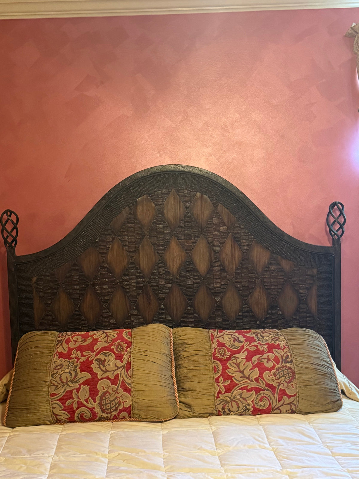 Close-up of ornately carved dark wooden headboard with spindle and lattice details against pink wall