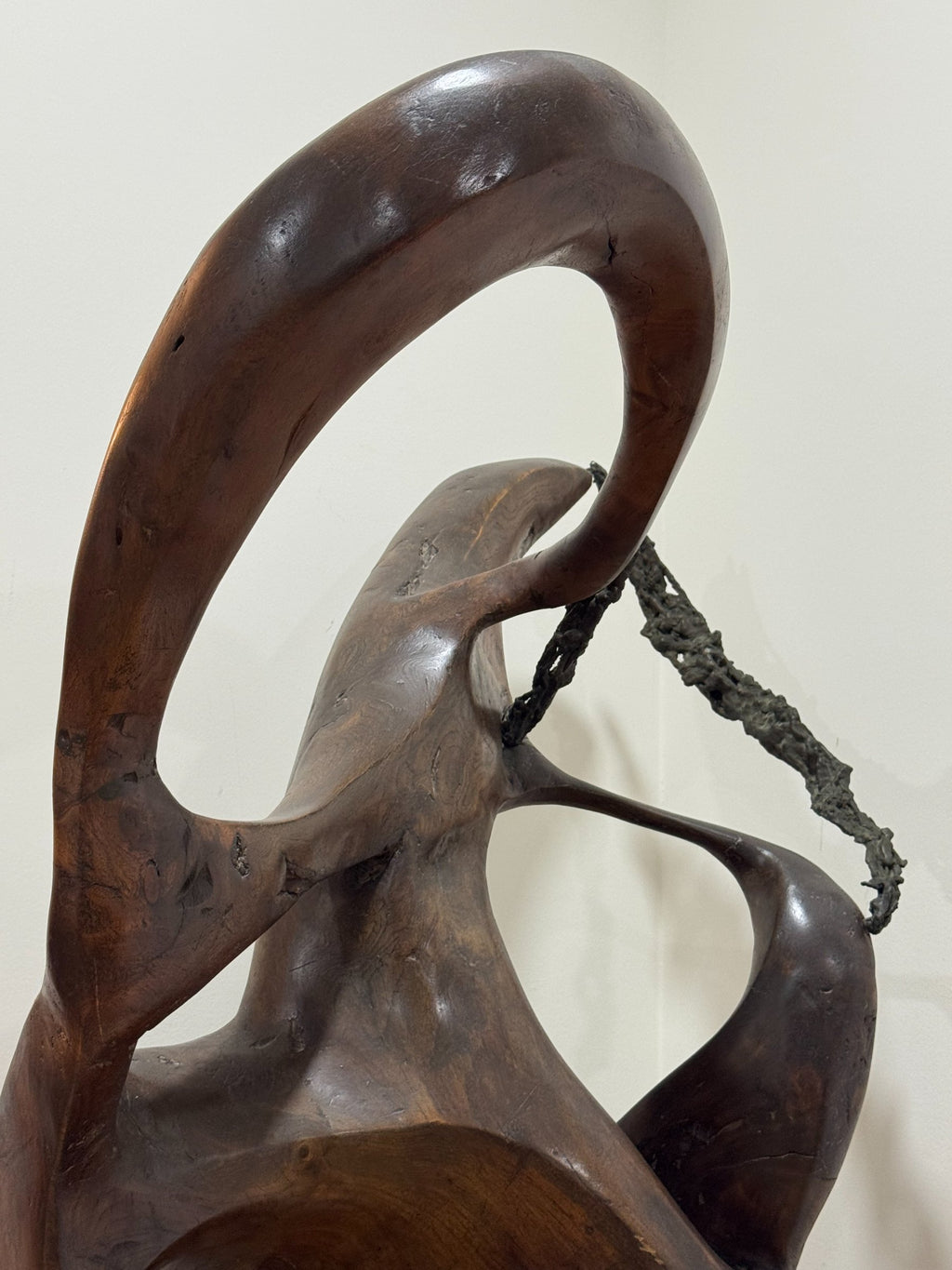 Full sculpture displayed in interior setting against white wall, tall abstract form on black pedestal, side profile perspective