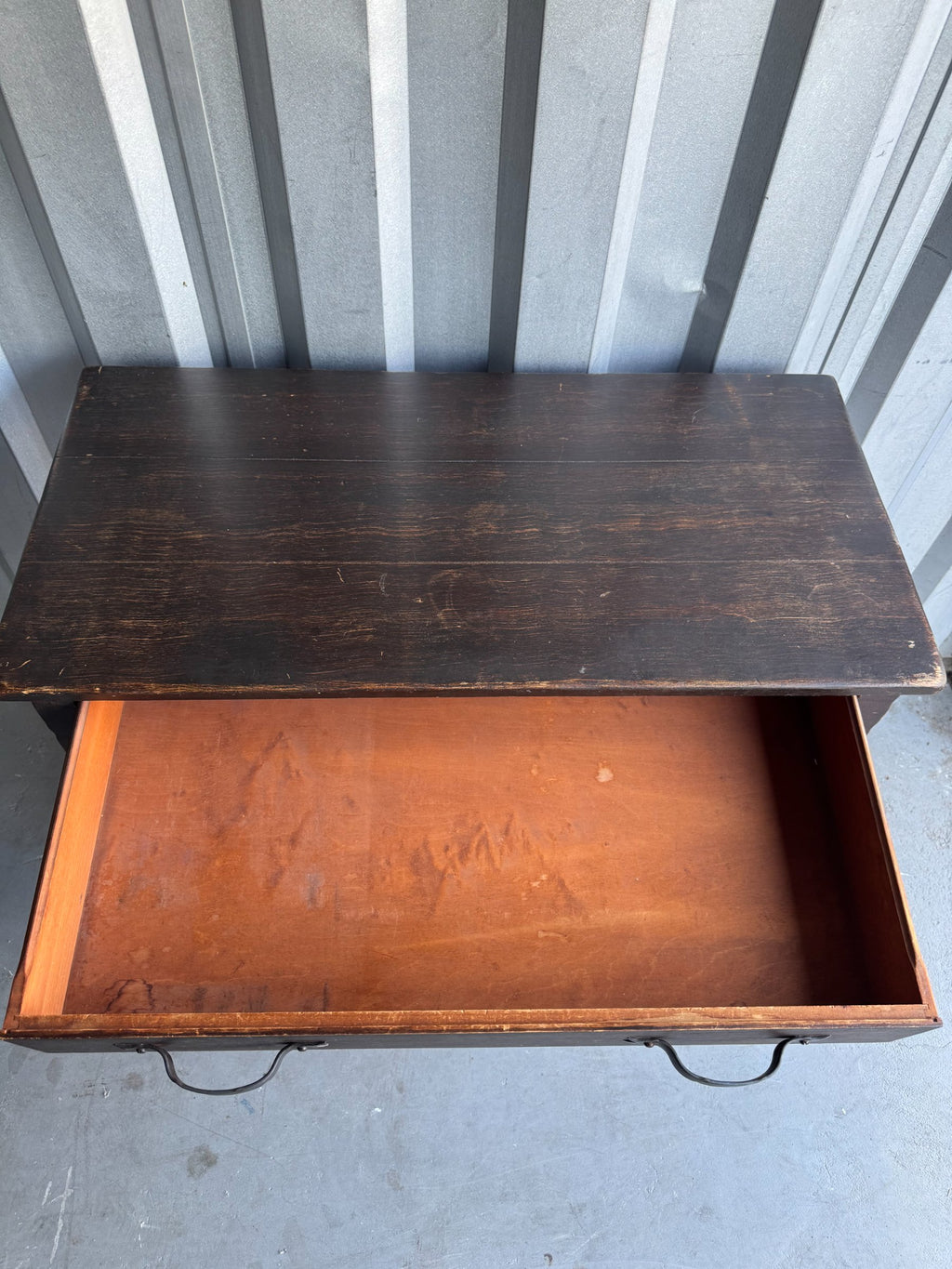 Overhead view of desk top showing dark wood grain, worn finish with lighter areas, closed drawer