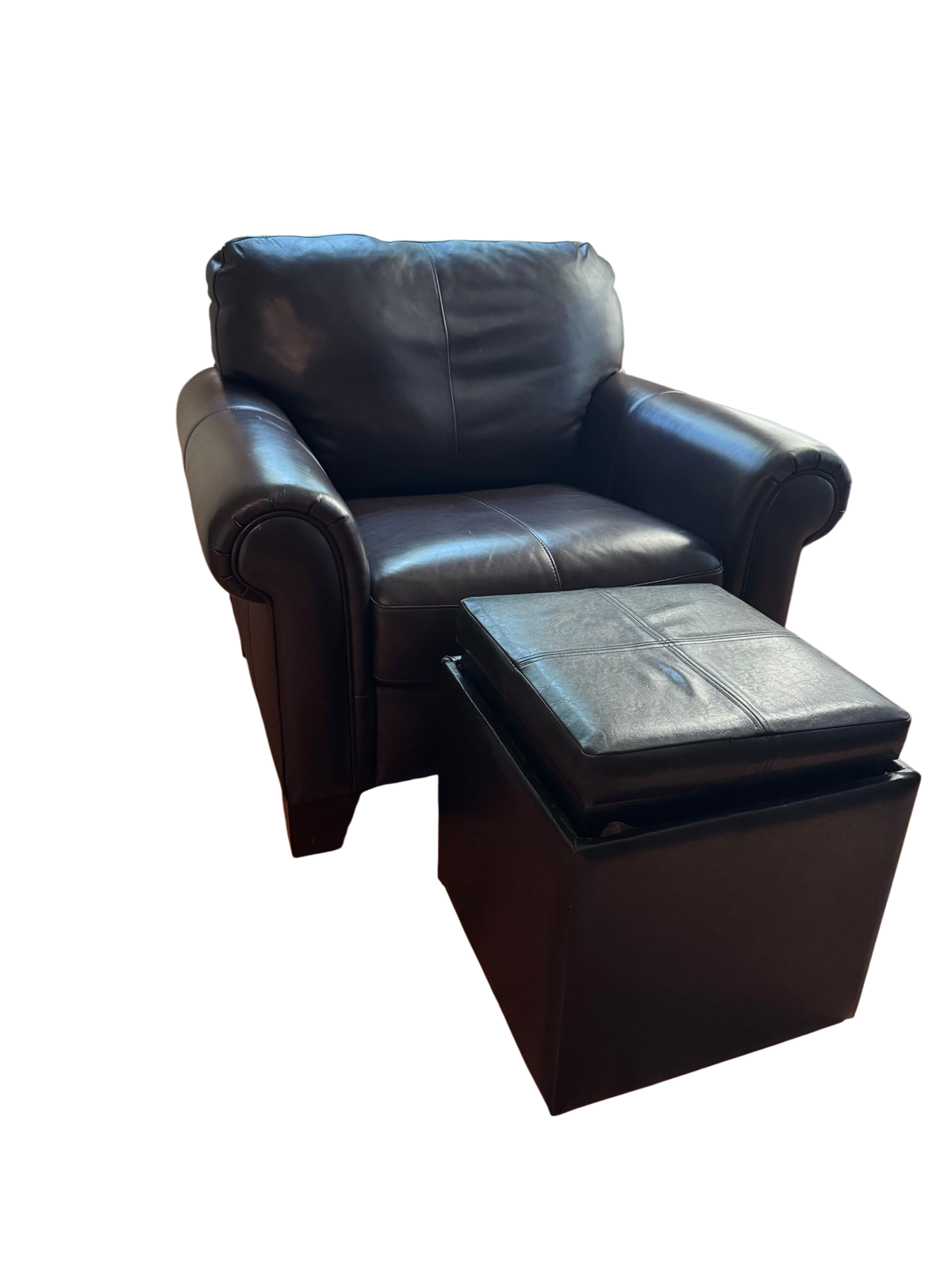 Black leather club chair with rolled arms next to a matching storage ottoman with lifted lid, in a living room with wood floors and shuttered windows