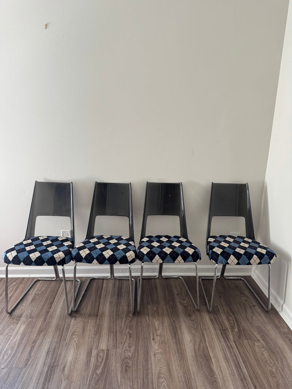 Set of four chairs lined up against white wall, showing black plastic backs and argyle patterned seats from front