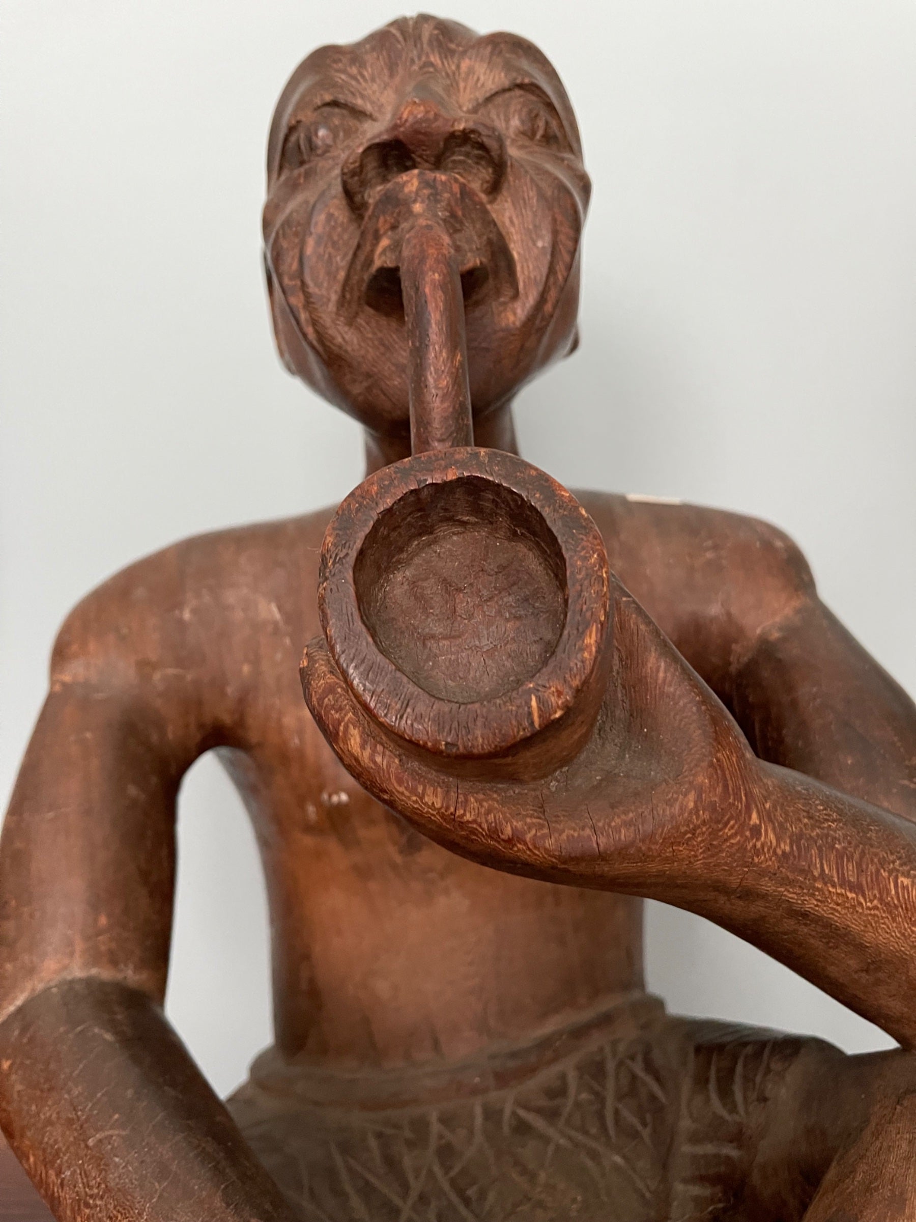 Close-up of figure's head and shoulders, mouth open around horn instrument, detailed facial carving