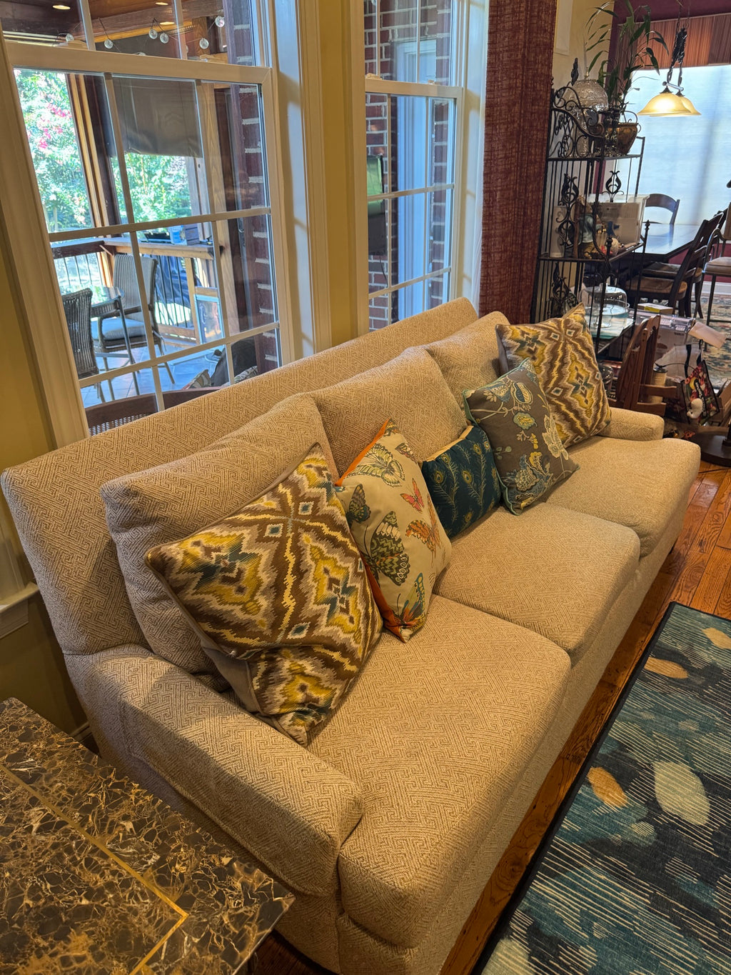 Angled view of sofa from above showing three cushions, oatmeal upholstery, and four coordinating decorative pillows with geometric and botanical prints