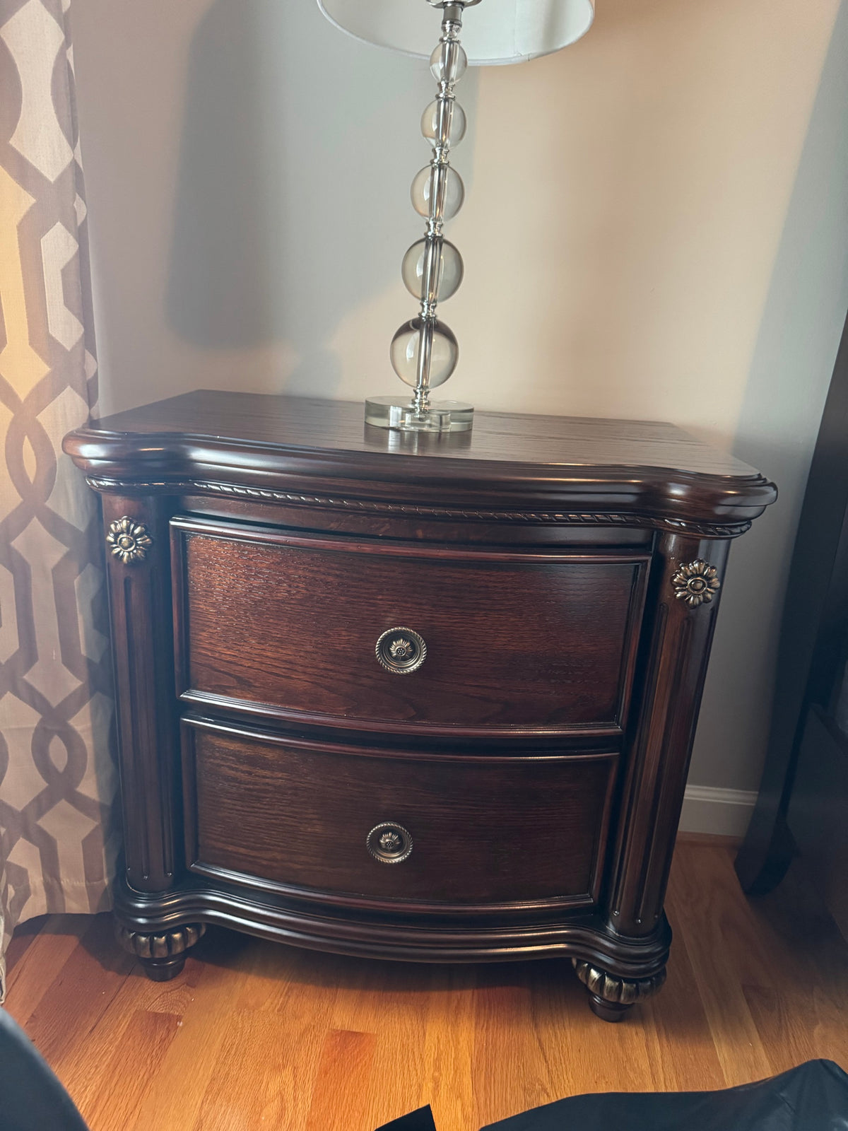 Dark cherry brown two-drawer Havertys nightstand with carved corner posts and floral metal pulls, shown with a table lamp on top