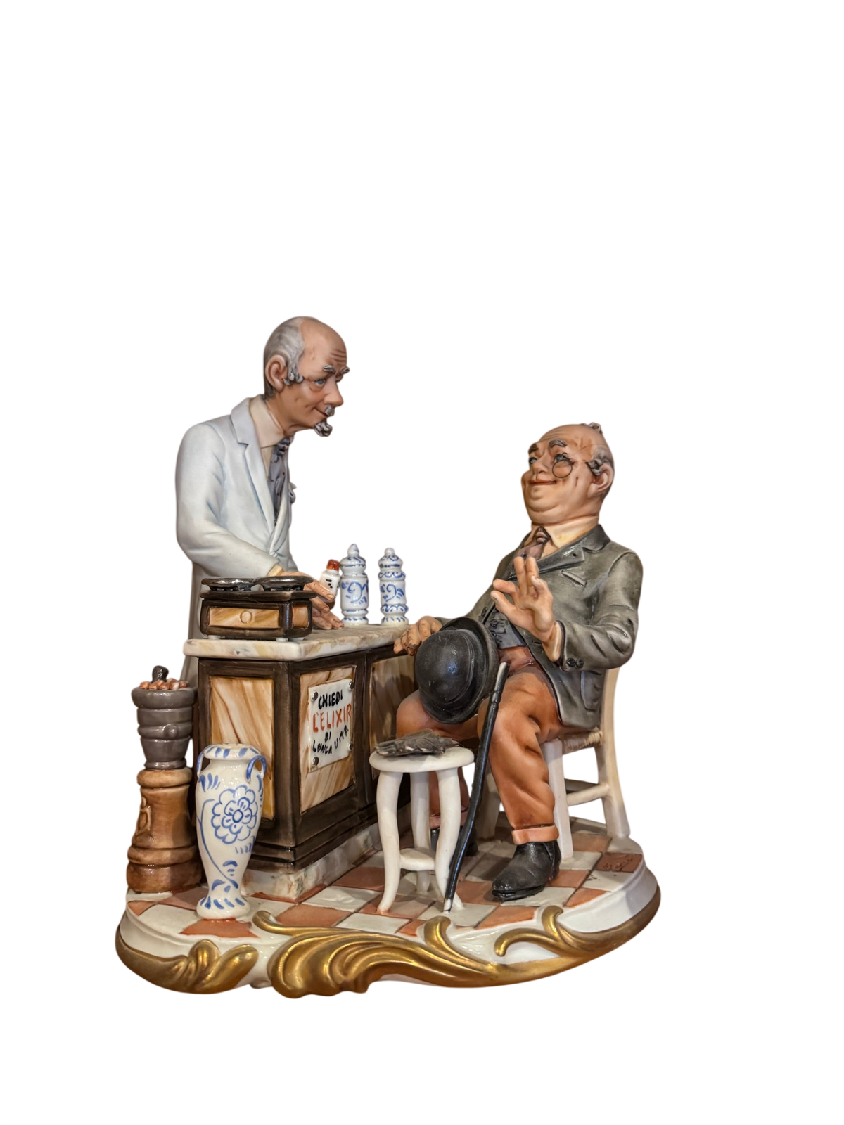Capodimonte-style porcelain figurine depicting pharmacy scene with two men, one standing at counter, one seated, gilt scrollwork base, blue and white ceramic details